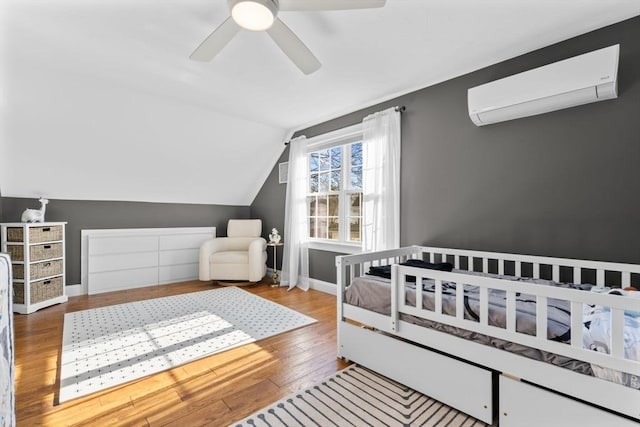 bedroom featuring lofted ceiling, an AC wall unit, ceiling fan, light hardwood / wood-style flooring, and a nursery area