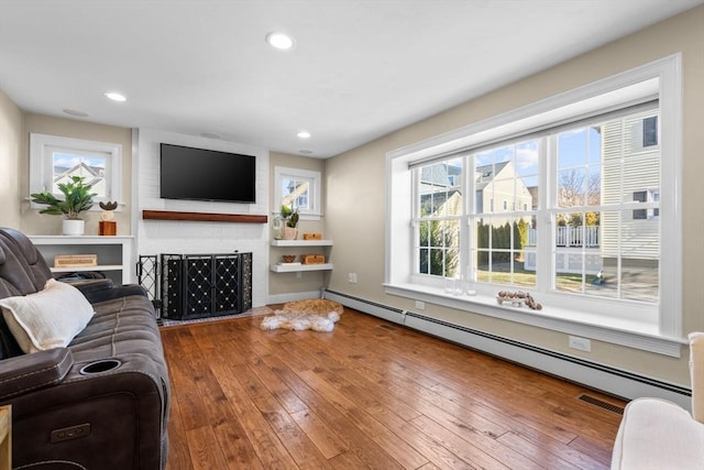 living room featuring a baseboard heating unit, a fireplace, and wood-type flooring