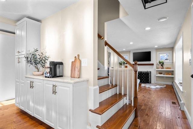 stairs with a brick fireplace, hardwood / wood-style floors, and a baseboard radiator