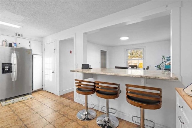 kitchen with kitchen peninsula, stainless steel fridge, a breakfast bar, a textured ceiling, and white cabinets