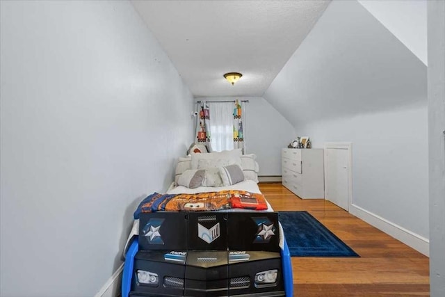 bedroom with hardwood / wood-style floors, a baseboard radiator, and lofted ceiling