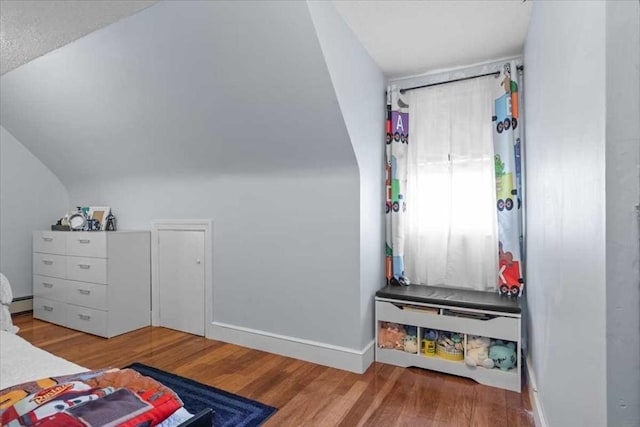 bedroom featuring a baseboard heating unit, vaulted ceiling, and light wood-type flooring