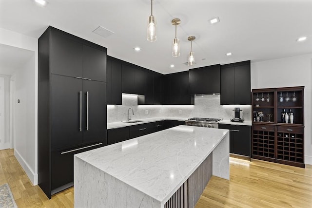 kitchen with dark cabinetry, a sink, hanging light fixtures, a kitchen island, and recessed lighting