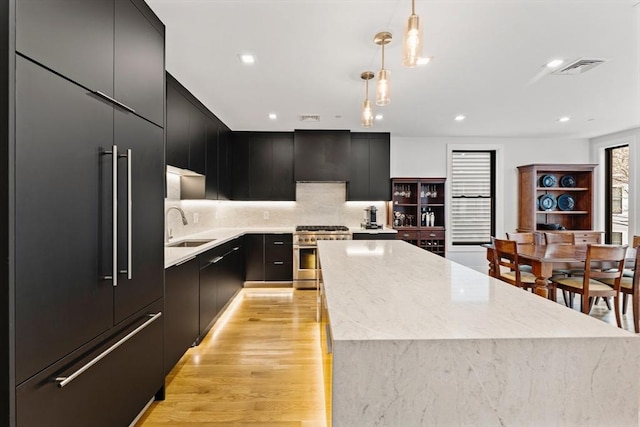 kitchen featuring stainless steel stove, dark cabinets, a sink, a kitchen island, and modern cabinets