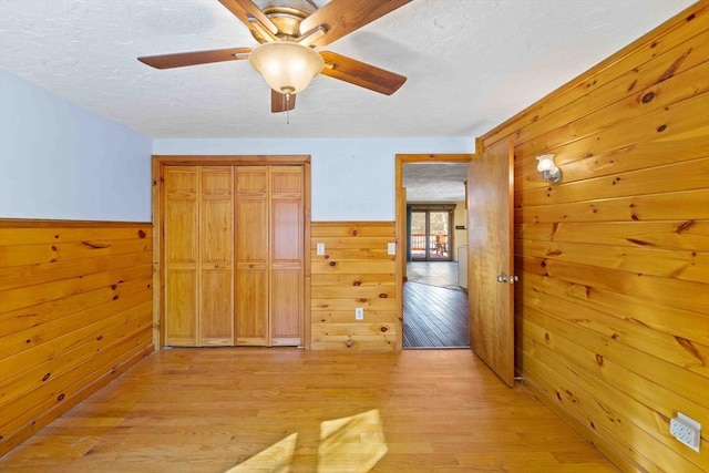 hallway featuring wood walls, light wood-style floors, and wainscoting