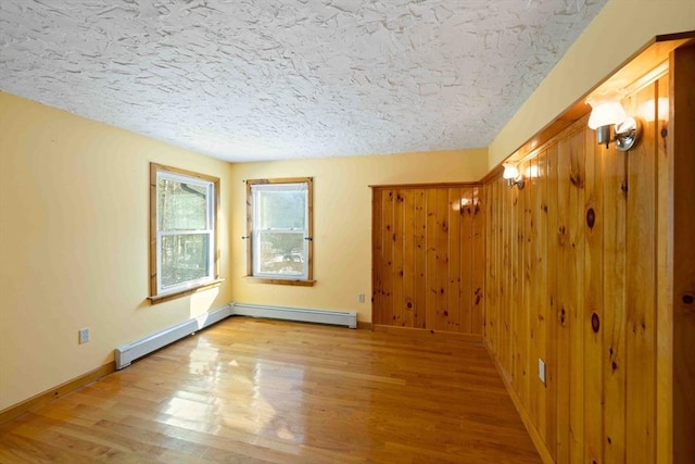 empty room featuring a textured ceiling, baseboards, baseboard heating, and wood finished floors