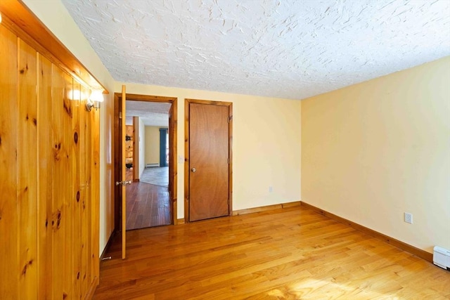 spare room featuring light wood-style flooring, baseboards, and a textured ceiling