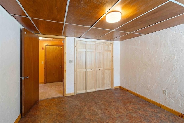 unfurnished bedroom featuring a textured wall, a closet, wood ceiling, and baseboards