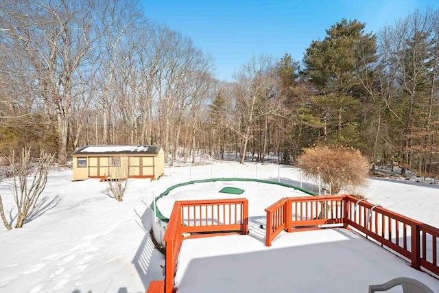 snow covered deck with a storage shed, fence, and an outbuilding