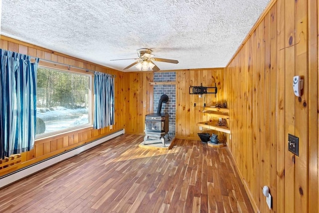 interior space featuring a baseboard heating unit, a wood stove, wooden walls, a textured ceiling, and hardwood / wood-style floors