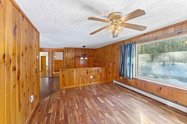 spare room featuring a baseboard radiator, wooden walls, a textured ceiling, and wood finished floors