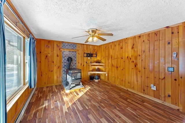 unfurnished living room with a baseboard heating unit, a wood stove, ceiling fan, a textured ceiling, and wood finished floors