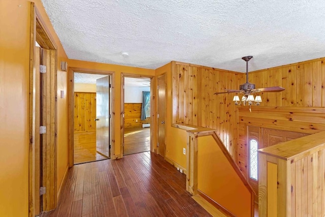 hall featuring an upstairs landing, wood walls, a textured ceiling, and hardwood / wood-style floors