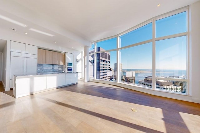 interior space featuring a healthy amount of sunlight, a water view, a wall of windows, and light hardwood / wood-style flooring