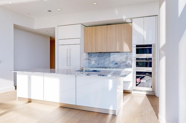 kitchen featuring light stone countertops, light brown cabinets, paneled refrigerator, tasteful backsplash, and white cabinets