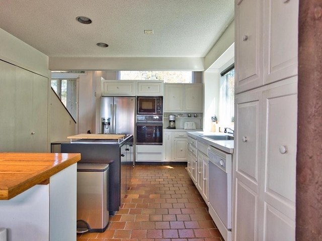 kitchen with black appliances, wood counters, a textured ceiling, a kitchen island, and a sink