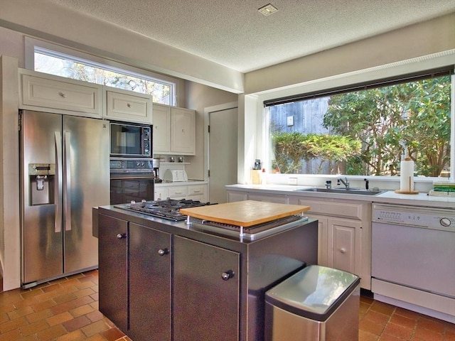 kitchen featuring black appliances, a sink, a kitchen island, brick flooring, and a textured ceiling