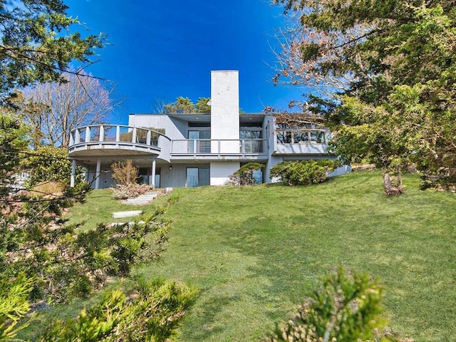 rear view of house featuring a chimney, a lawn, and a balcony