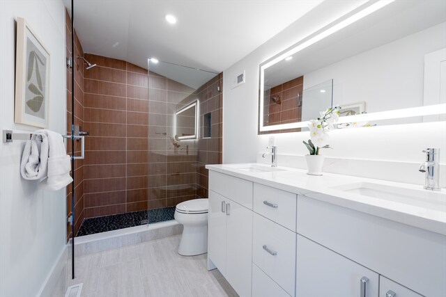 bathroom with a tile shower, vaulted ceiling, dual bowl vanity, toilet, and tile patterned flooring