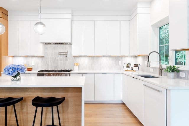 kitchen featuring white cabinetry, backsplash, light hardwood / wood-style floors, decorative light fixtures, and sink