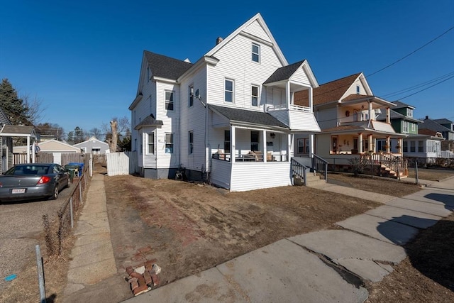 view of front of property with a residential view, a balcony, a shingled roof, and fence