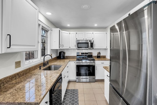 kitchen featuring light stone countertops, white cabinets, stainless steel appliances, sink, and light tile patterned floors