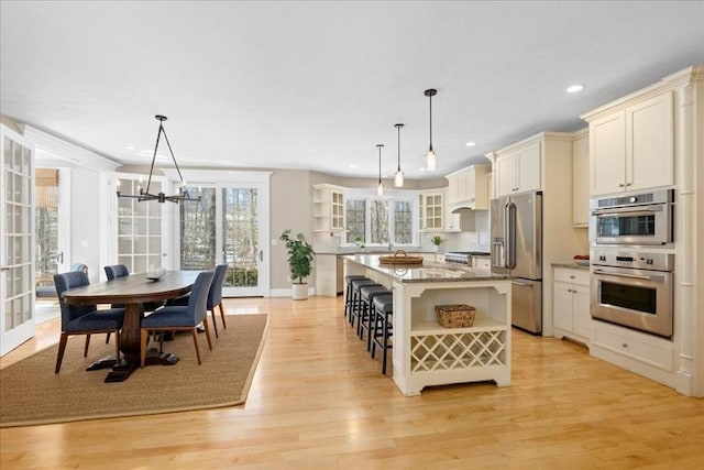 kitchen with stainless steel appliances, light wood-style flooring, glass insert cabinets, light stone countertops, and a kitchen breakfast bar