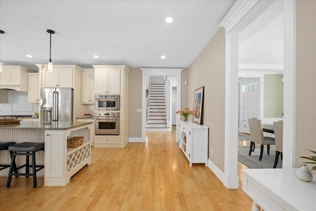 kitchen featuring a kitchen breakfast bar, hanging light fixtures, appliances with stainless steel finishes, light wood-type flooring, and backsplash