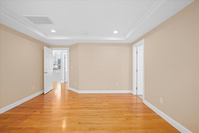 empty room with light wood-style flooring, a tray ceiling, and ornamental molding