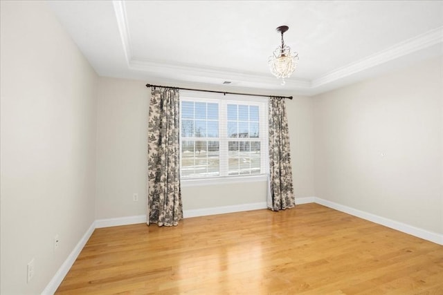 empty room featuring light wood-style floors, a tray ceiling, and ornamental molding