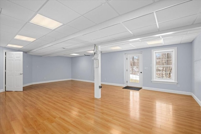 below grade area with a drop ceiling, light wood-type flooring, and baseboards