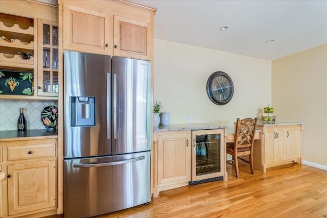 kitchen with stainless steel fridge, light brown cabinets, beverage cooler, light wood finished floors, and tasteful backsplash