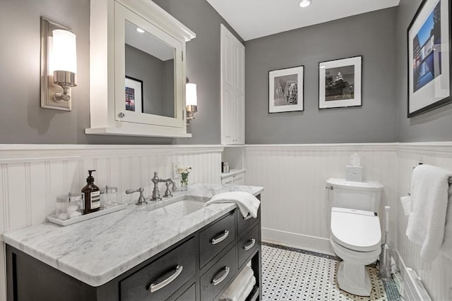 bathroom with wainscoting, toilet, a decorative wall, and vanity