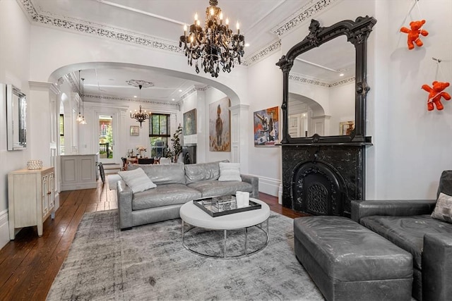 living room with a chandelier, ornamental molding, dark wood-type flooring, arched walkways, and a fireplace
