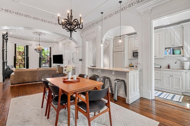 dining room with arched walkways, dark wood-type flooring, a chandelier, and crown molding