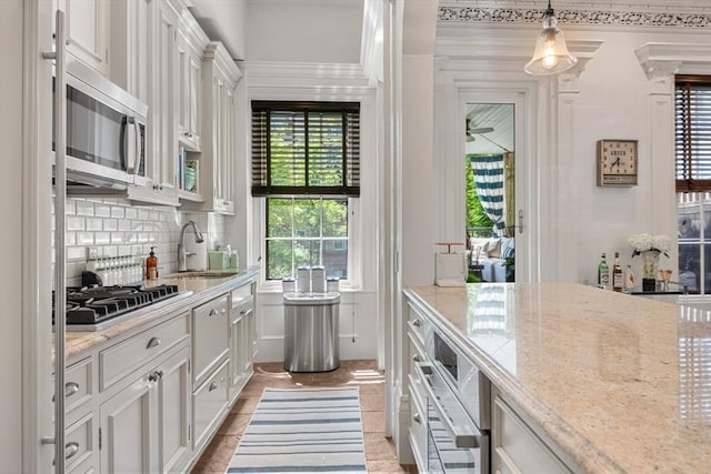 kitchen with stainless steel appliances, white cabinetry, a sink, backsplash, and light stone countertops
