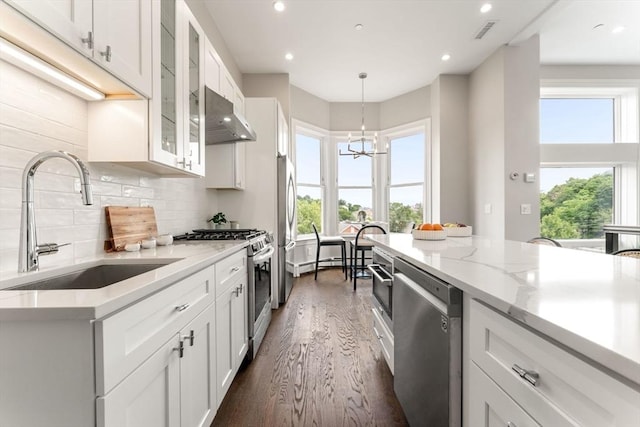 kitchen with sink, dark wood-type flooring, stainless steel appliances, a chandelier, and white cabinets