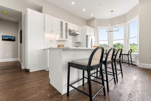 kitchen with kitchen peninsula, stainless steel fridge, dark hardwood / wood-style flooring, white cabinets, and a chandelier