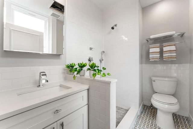 bathroom featuring tile patterned flooring, tiled shower, toilet, vanity, and tile walls