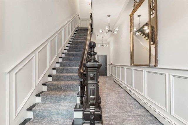 staircase featuring a baseboard heating unit, a towering ceiling, carpet floors, and a notable chandelier