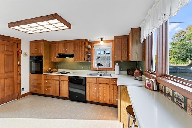 kitchen featuring under cabinet range hood, light countertops, brown cabinets, black appliances, and a sink