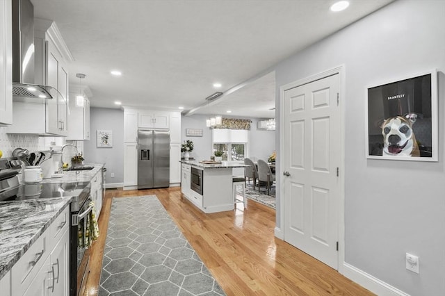 kitchen with a breakfast bar, a sink, stainless steel appliances, white cabinets, and wall chimney exhaust hood