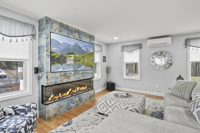 living room with baseboards, a lit fireplace, wood finished floors, and a wall mounted AC