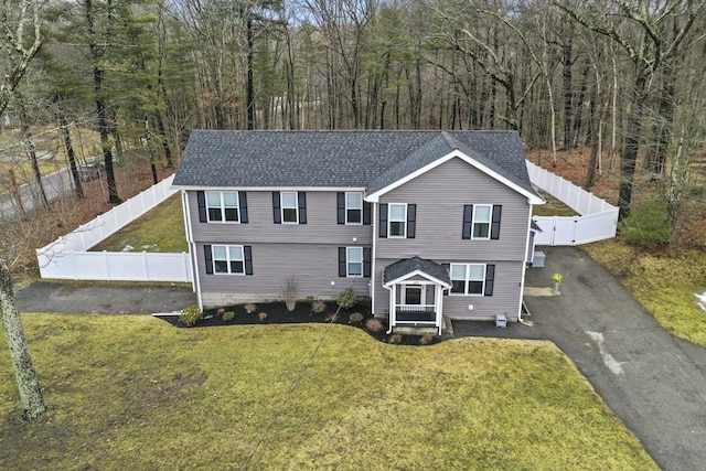 view of front of house featuring aphalt driveway, a front yard, a fenced backyard, and a shingled roof