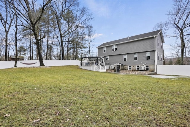 rear view of house with stone siding, a fenced backyard, a yard, a wooden deck, and stairs