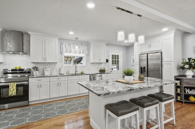 kitchen featuring a sink, a kitchen breakfast bar, appliances with stainless steel finishes, wall chimney exhaust hood, and light wood finished floors