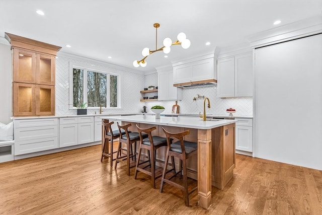 kitchen with light countertops, backsplash, light wood-style floors, an island with sink, and a kitchen breakfast bar