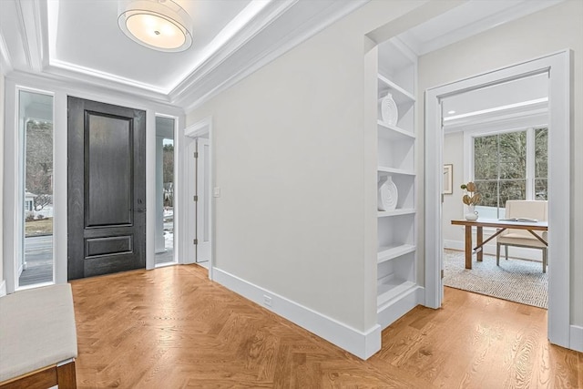 foyer with a raised ceiling, crown molding, and baseboards