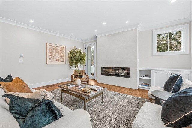 living room featuring recessed lighting, a fireplace, baseboards, ornamental molding, and light wood-type flooring