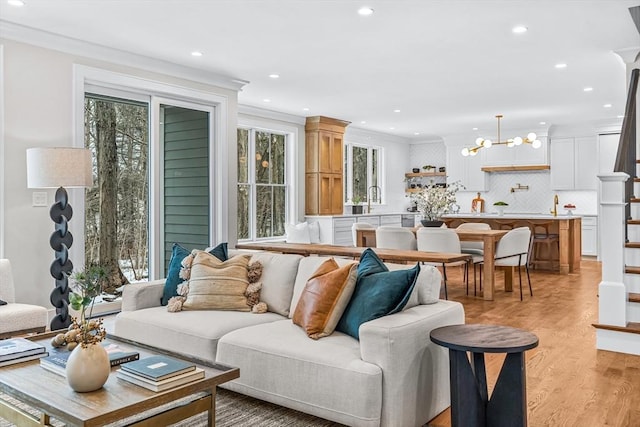 living area featuring light wood-style flooring, recessed lighting, a notable chandelier, ornamental molding, and stairway